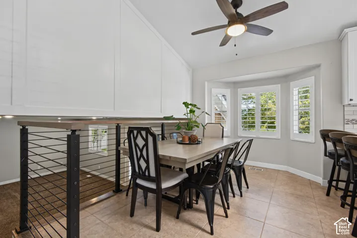 Vaulted ceiling with a wood-finish ceiling fan, bay window with plantation shutters, cable railing system with wood-finish top rail, and tile flooring