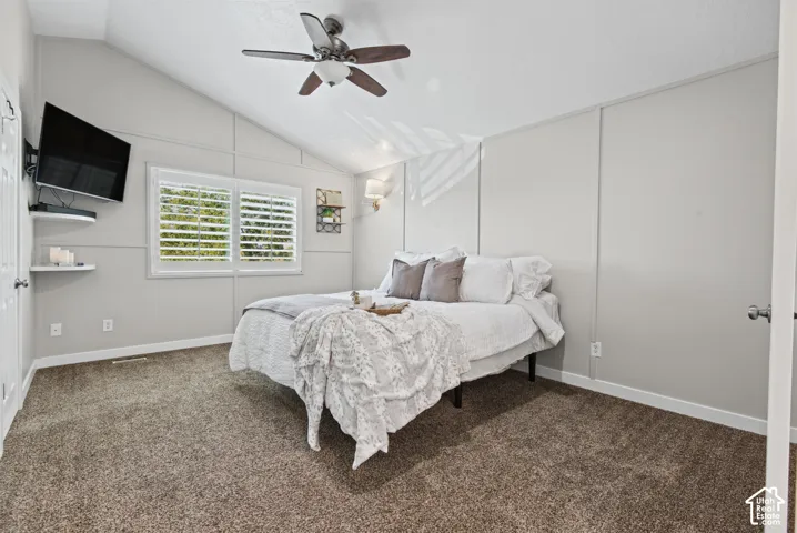 Vaulted ceiling with a ceiling fan light fixture, wall paneling, plantation shutters on windows, and carpet flooring