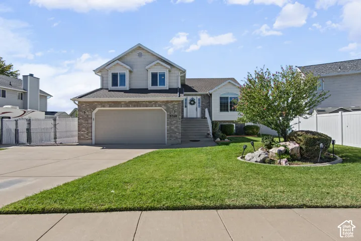 Tri-level residence featuring a two-car garage, brick and siding exterior, concrete driveway, and front lawn with a decorative rock garden