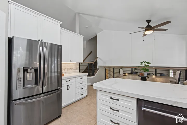 White shaker-style cabinetry with dark hardware, stainless steel refrigerator, white countertop island, and wood-finish ceiling fan