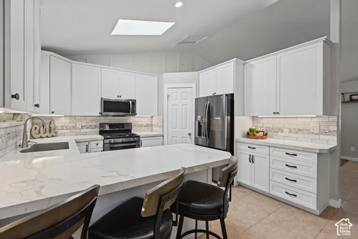 Spacious kitchen featuring an expansive island, white cabinetry, stainless steel appliances, and a skylight