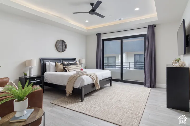 Recessed ceiling lighting with a tray ceiling, ceiling fan, sliding glass door, and wood-finish flooring
