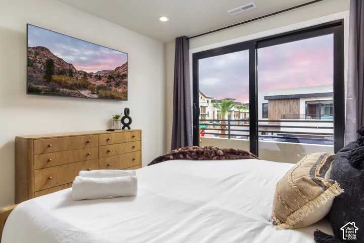 Built-in wall-mounted television, wood-finish dresser with brass hardware, recessed ceiling light, and sliding glass balcony door with dark trim