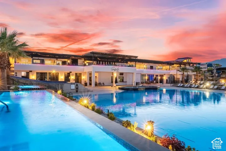 Expansive resort-style swimming pools with integrated lighting, a multi-level clubhouse structure, and outdoor lounge areas