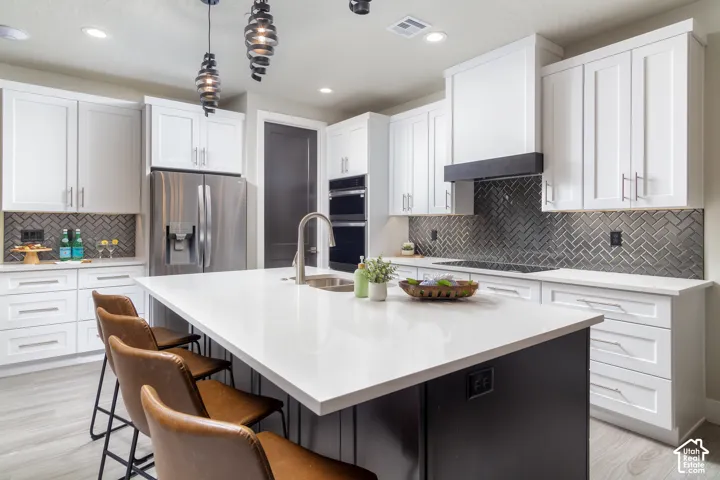 White shaker cabinetry, stainless steel appliances, herringbone tile backsplash, white countertops, and wood-finish flooring