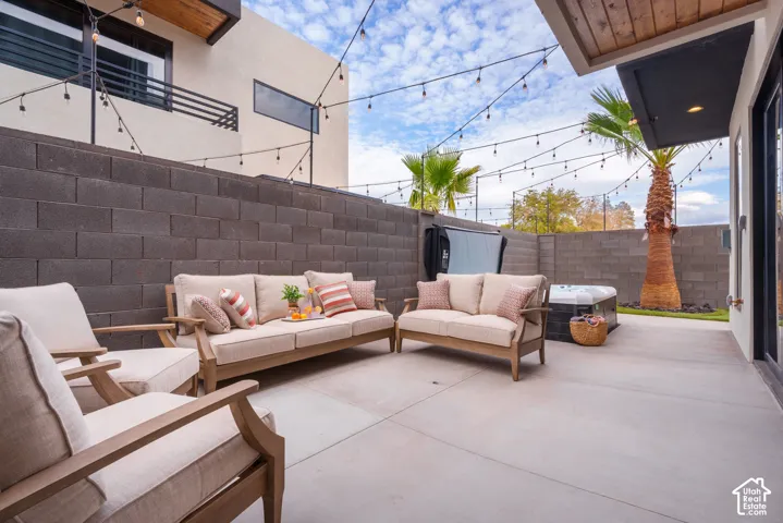 Concrete patio with string lighting, dark concrete block wall, and integrated hot tub