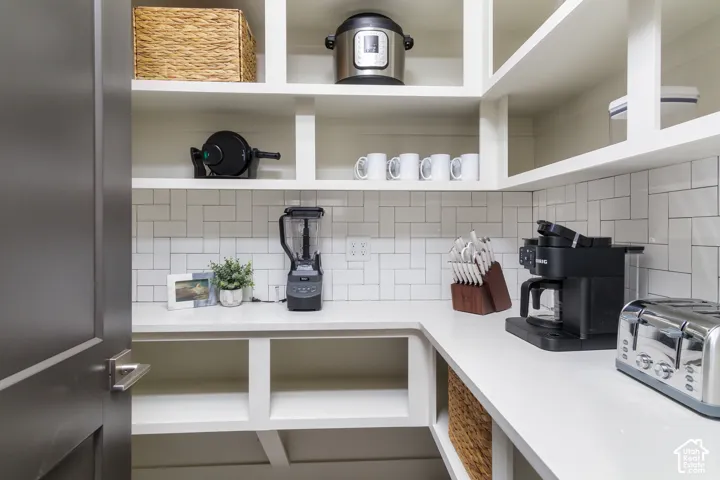 Built-in shelving, white subway tile backsplash, white countertops, and a dark wood door with brushed nickel hardware