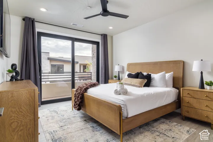 Sliding glass doors opening to an exterior balcony with metal railing, ceiling fan with integrated lighting, recessed ceiling lights, and wood-finish flooring