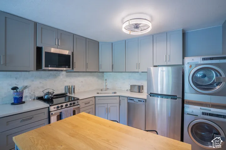 Gray shaker-style cabinetry, stainless steel appliances, light-toned countertops, tile backsplash, and wood-finish island top