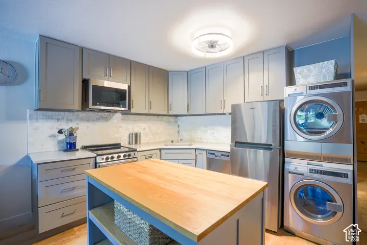 Gray cabinetry with stainless steel appliances, butcher block island, and stacked washer and dryer