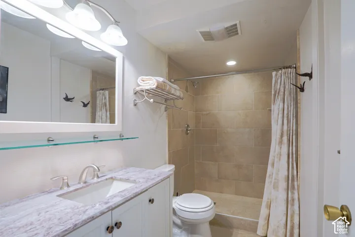 Vanity with an integrated sink and brushed nickel faucet, a large framed mirror with overhead lighting, a glass shelf, and a shower with tiled walls