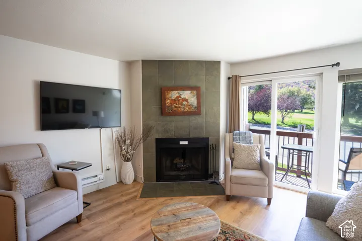 Corner fireplace with tile surround, wood-finish flooring, and a sliding glass door to an outdoor balcony