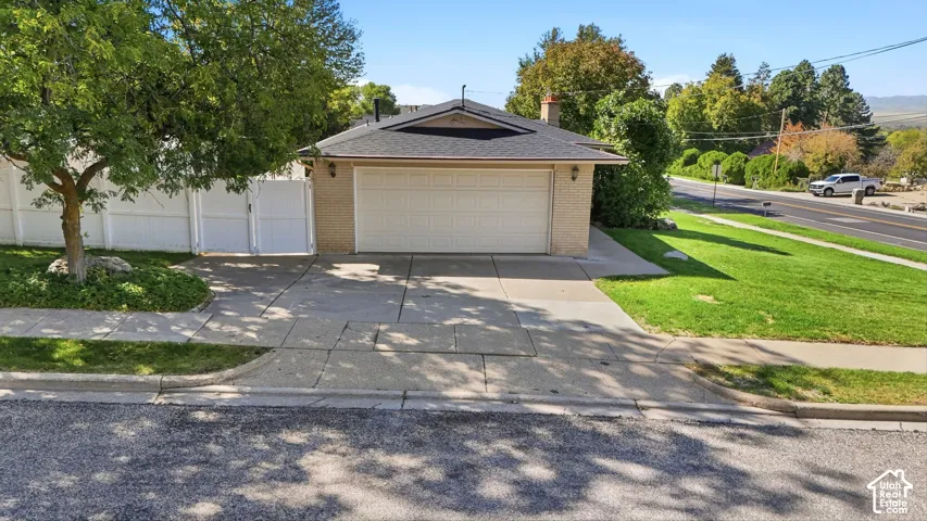 Brick exterior, attached garage, paved driveway, white privacy fence, and mature tree