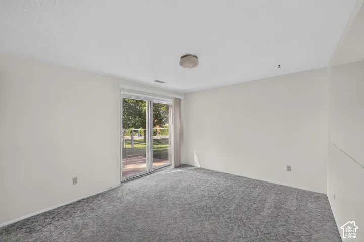 Sliding glass door leading to an outdoor space, light-toned walls, and grey patterned carpeting