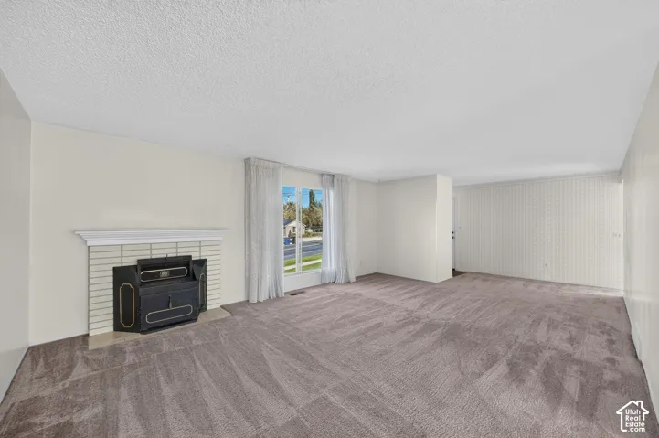 Spacious room with plush carpeting, a prominent fireplace with a white mantel, and a large window with white sheers