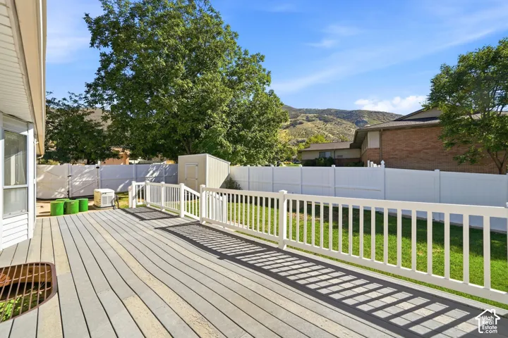 Expansive backyard featuring a composite deck, white vinyl fencing, a storage shed, and a manicured lawn