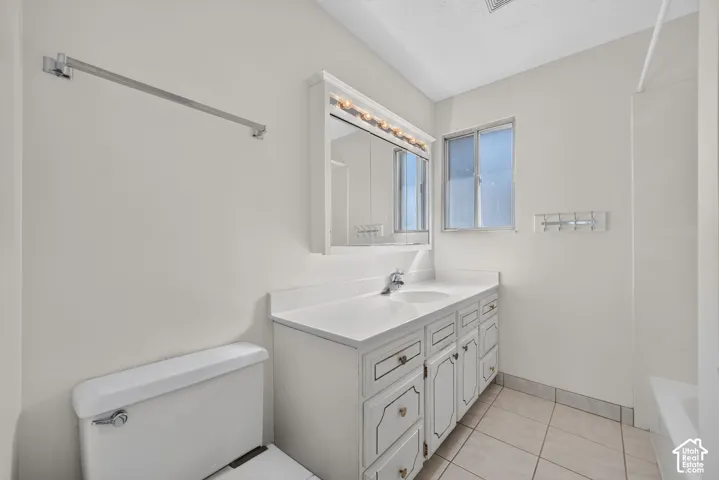 Vanity with integrated sink, wall-mounted medicine cabinet with integrated lighting, tiled flooring, toilet, and a window