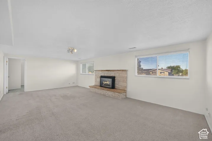 Spacious room featuring light-colored carpet, a stone-clad fireplace with a hearth, and multiple windows