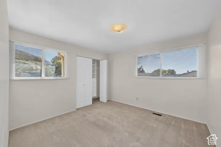 Neutral-toned wall paint, two large windows, track closet doors, and carpeted flooring