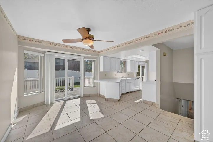 Tiled flooring extending into the kitchen, a ceiling fan with integrated lighting, and white cabinetry