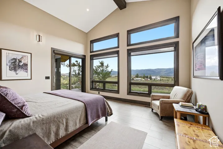 Vaulted ceiling with exposed wood beams, large picture windows, wood-finish flooring, and a sliding glass door