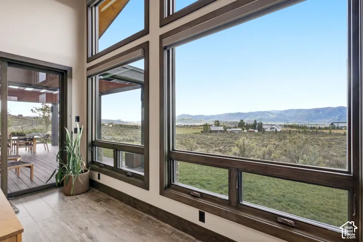 Full-height windows with dark frames, wood-finish flooring, and a sliding glass door to an outdoor deck with a built-in table