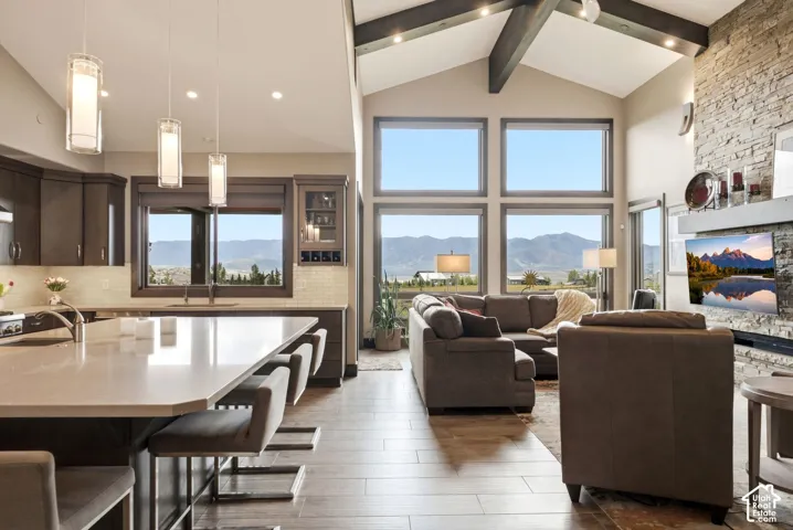 Kitchen island with seating, dark wood-finish cabinetry, vaulted ceiling with exposed beams, full-height stone-finish fireplace, and multi-pane windows