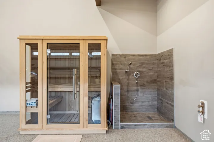 Built-in sauna with a glass-panel door, wood-finish interior, and an adjacent walk-in shower featuring gray tile surround and a chrome shower fixture