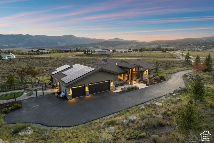 Expansive mountain scenery, modern architecture, solar panel installation, attached three-car garage, and a winding paved driveway