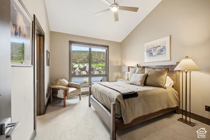 Vaulted ceiling, ceiling fan, expansive window, neutral wall tones, carpeted flooring