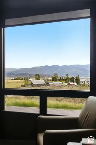 Expansive window with roller shade, offering broad scenery of distant mountains, open fields, and residential structures