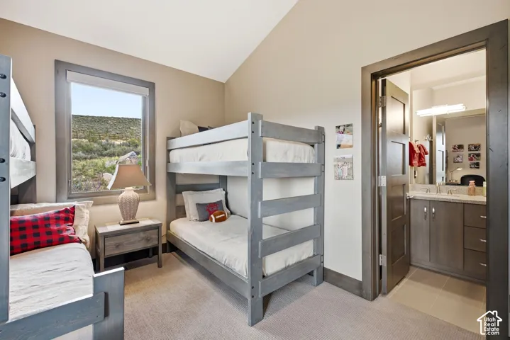 Neutral wall paint, vaulted ceiling, light-toned carpet, built-in bunk beds, and an en-suite bathroom with a double vanity
