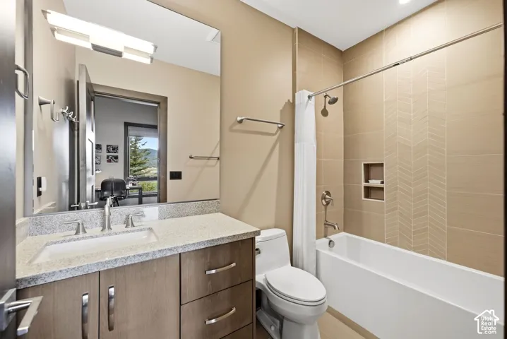 Bathroom featuring a vanity with an integrated sink, a light-colored countertop, wood-finish cabinetry with brushed nickel pulls, and a built-in shower niche with a herringbone tile pattern