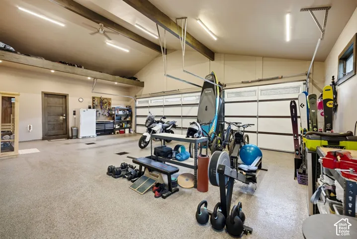 Attached garage with a high vaulted ceiling, exposed wood beams, and a ceiling fan