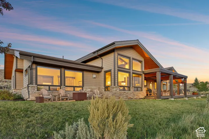 Contemporary exterior featuring warm-toned siding, extensive window arrays, a covered outdoor patio, and stone accents