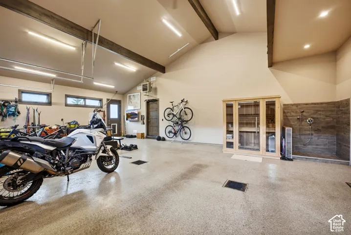 Spacious garage with high vaulted ceilings, exposed wood beams, and a durable epoxy-coated concrete floor