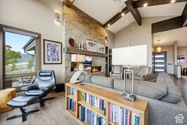 Vaulted ceiling with exposed wood beams, stone-clad fireplace, wood-finish flooring, and large window overlooking natural scenery