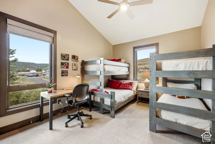Vaulted ceiling, two bunk bed structures, built-in desk, large window with roller shade, and ceiling fan