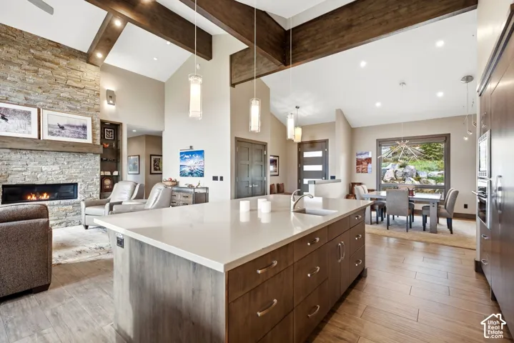 Open-concept living area featuring exposed wood beams, a stone-clad fireplace, and wood-finish flooring