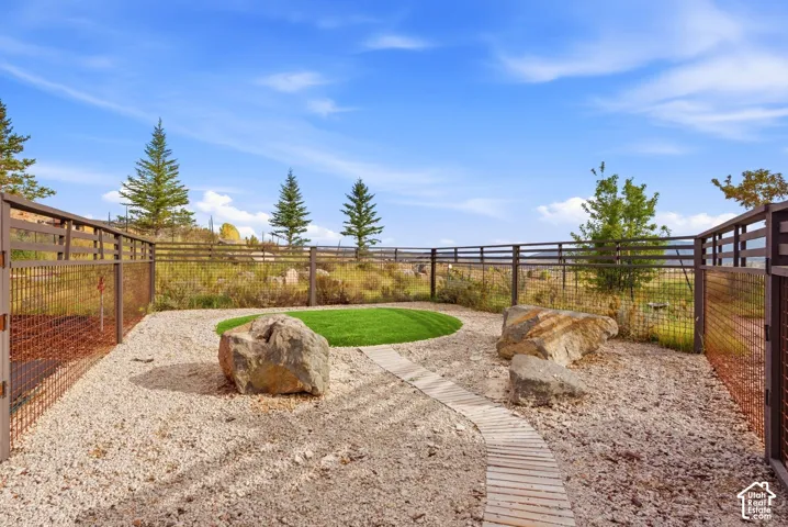 Landscaped outdoor area featuring a gravel ground cover, a circular artificial turf patch, a wooden pathway, and natural boulders