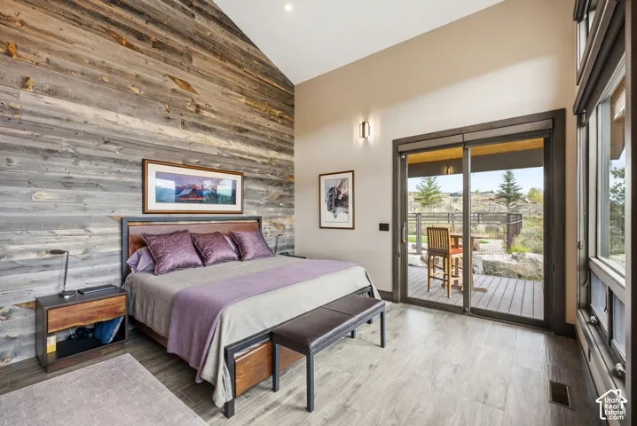 Vaulted ceiling with wood-clad accent wall, large sliding glass door with outdoor access, and wood-finish flooring