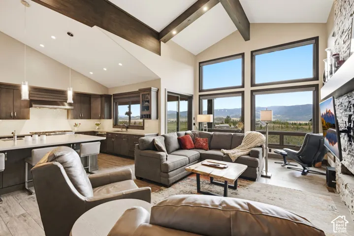 Vaulted ceilings with exposed beams, large windows, stone-clad fireplace, built-in kitchen cabinetry, and a kitchen island with bar seating
