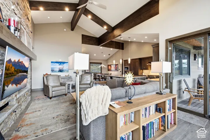Vaulted ceiling with exposed wood beams, stone-faced fireplace with wood mantel, recessed lighting, and sliding glass door leading to an outdoor patio