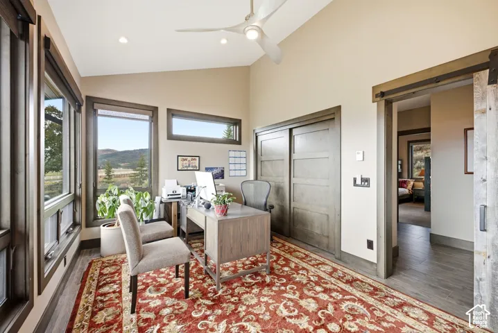 Vaulted ceiling with a ceiling fan, multiple windows with dark trim, wood-finish flooring, and a sliding barn door