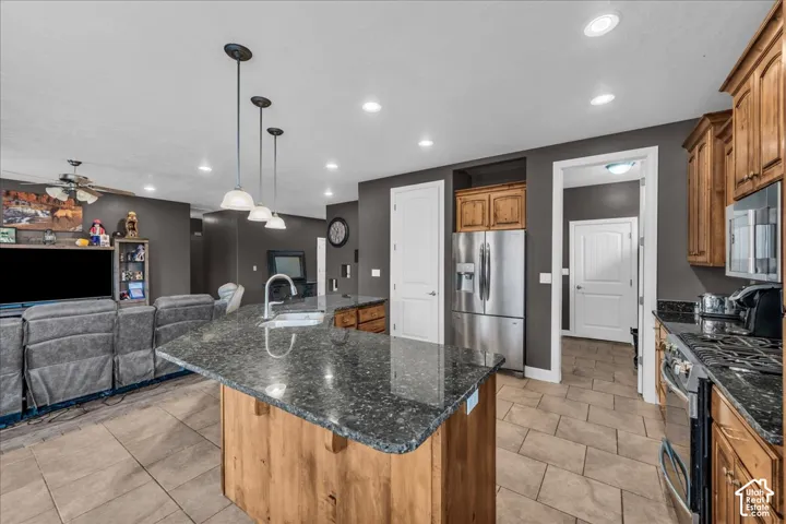 Kitchen island with dark countertop, stainless steel appliances, wood cabinetry, recessed lighting, and tile flooring