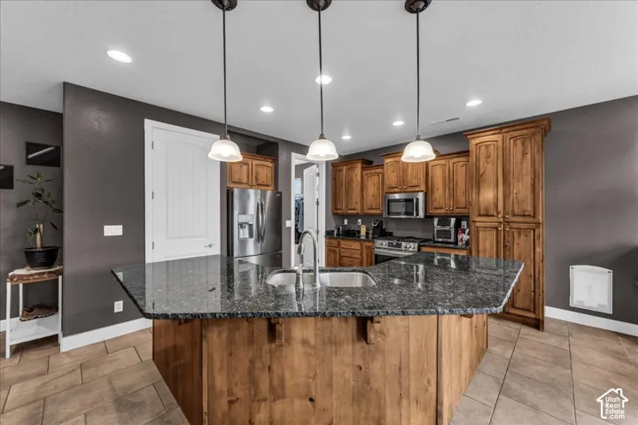 Kitchen featuring a large island with an integrated sink, dark speckled countertop, and pendant lighting