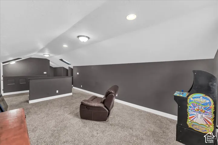 Carpeted loft space with vaulted ceiling, recessed lighting, skylights, and dark accent walls