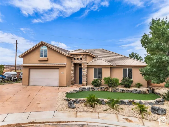 Stucco exterior featuring a stone-faced entry, an arched window, a two-car garage, and a low-maintenance landscape with artificial turf