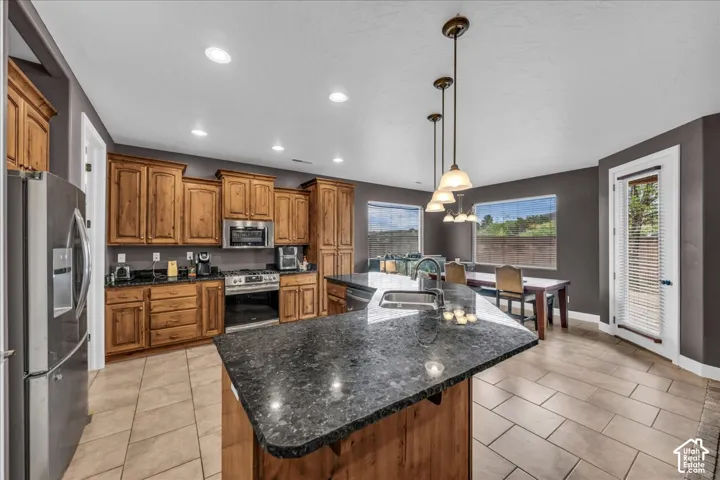 Kitchen featuring wood cabinetry, dark stone countertops, stainless steel appliances, and a central island with a sink
