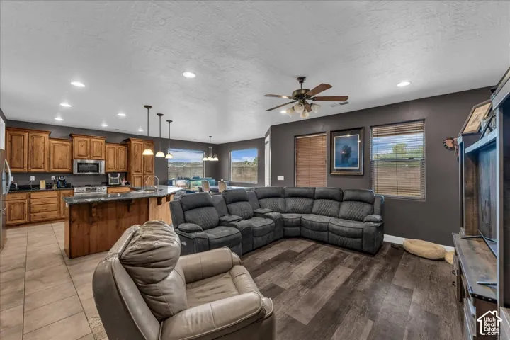 Expansive open-concept living area featuring wood-finish flooring, a ceiling fan, and large windows with blinds